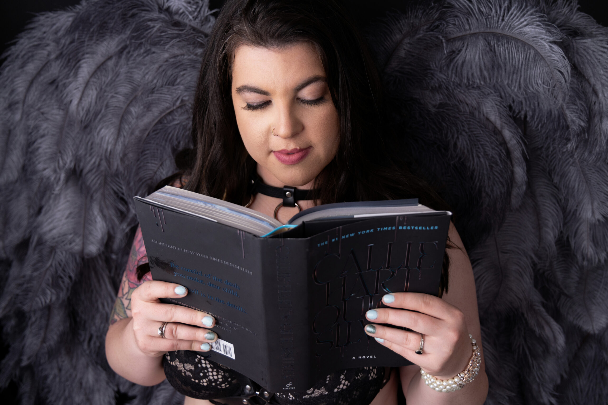 Woman reading book in moody boudoir studio Wenatchee Washington wearing angel wings