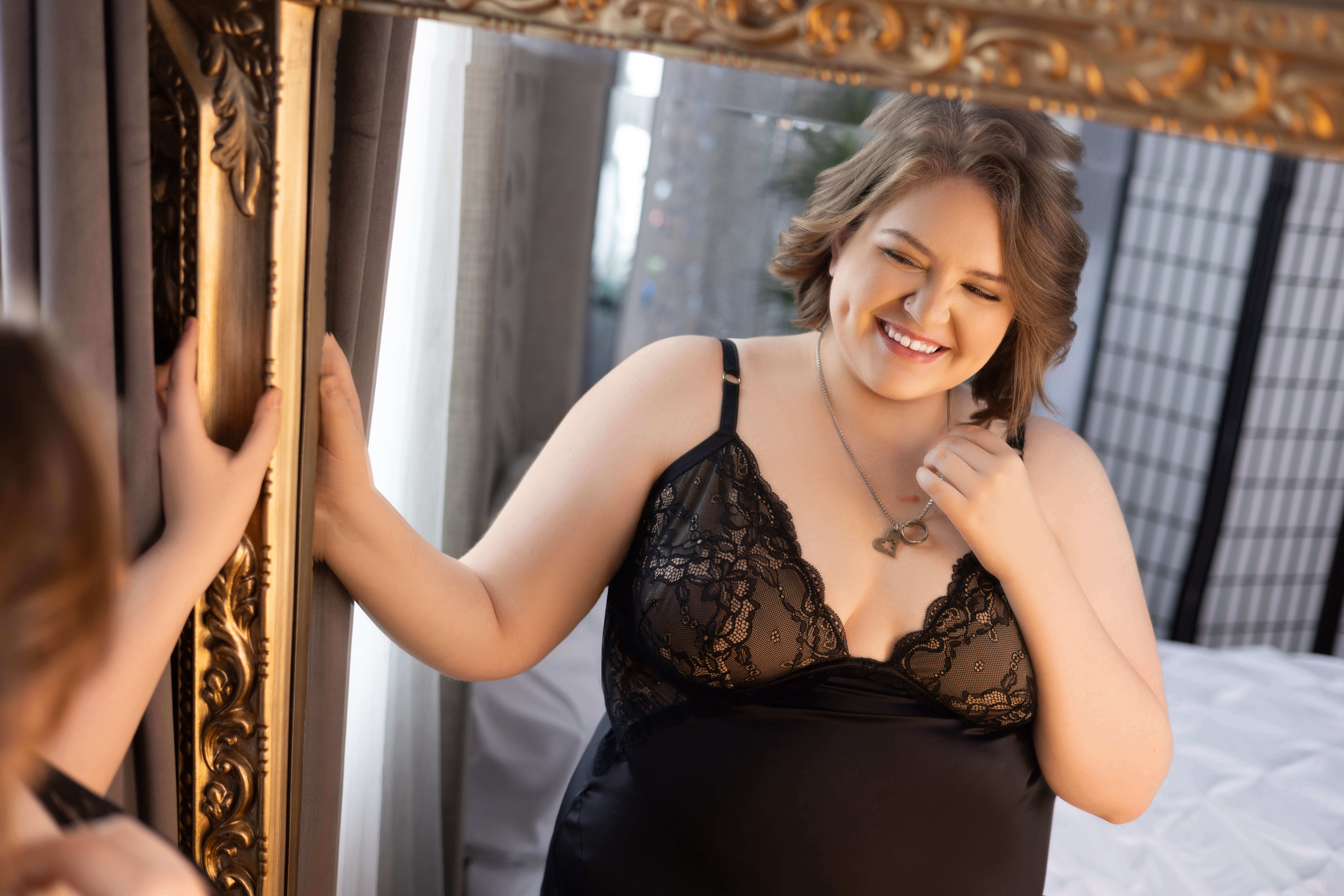 Woman in black lingerie smiling by a window during a private boudoir session in Wenatchee.